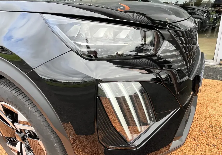 Gros plan sur l'avant droit noir brillant du Peugeot 2008 2024, mettant en valeur ses phares LED et la calandre distinctive.