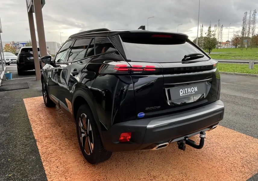 Vue 3/4 arrière droite du Peugeot 2008 noir 2024 avec feux LED allumés et attelage visible sur un sol orange.
