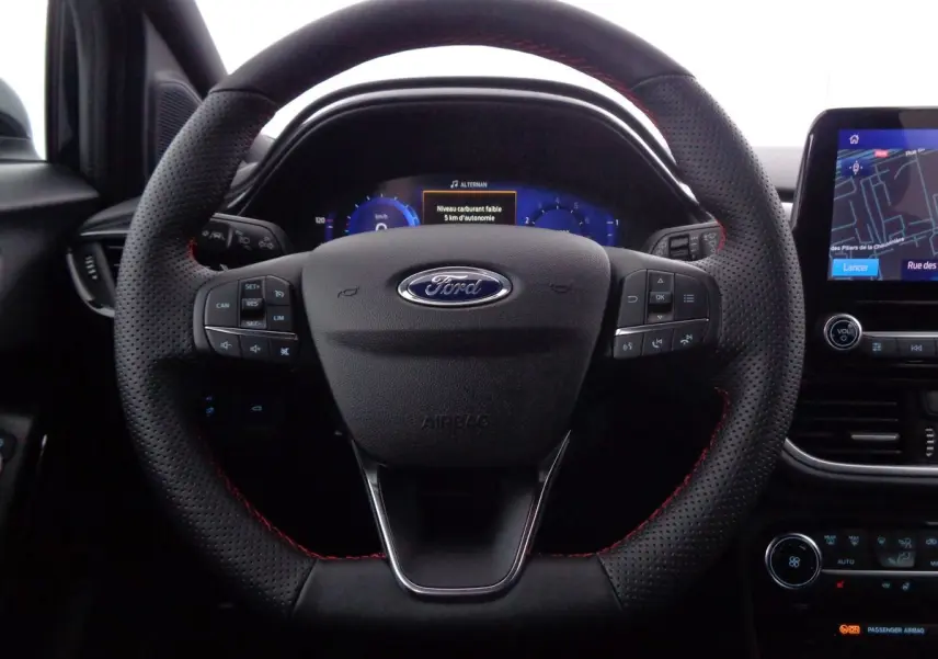 Vue rapprochée du volant en cuir noir avec surpiqûres rouges de la Ford Puma 2022, tableau de bord numérique et écran tactile visible.