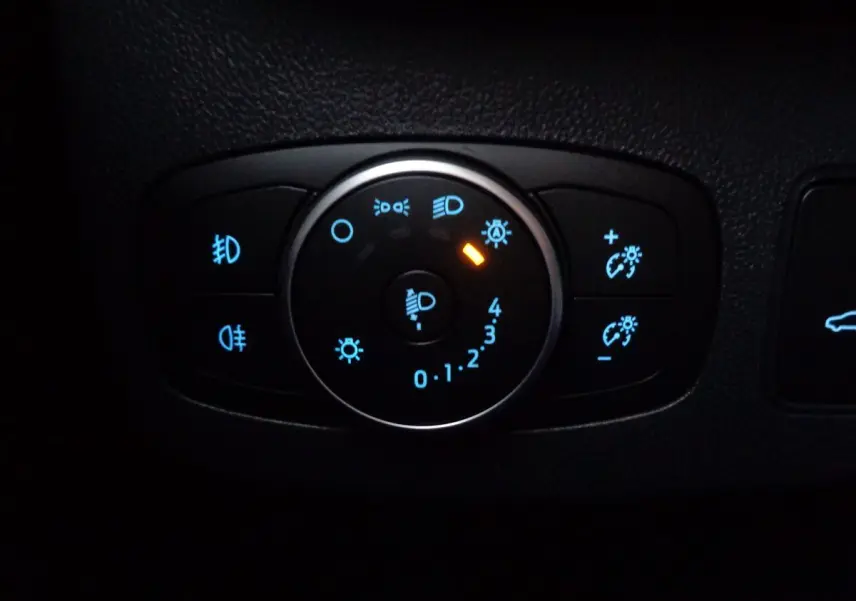 Gros plan sur le bouton de réglage des phares avec éclairage bleu et orange dans le Ford Puma noir Agate 2022.