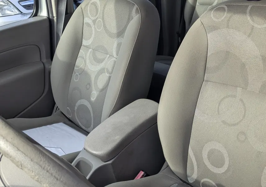 Vue intérieure des sièges avant gris à motifs ronds du Renault Kangoo II bleu ciel, avec accoudoir central visible.