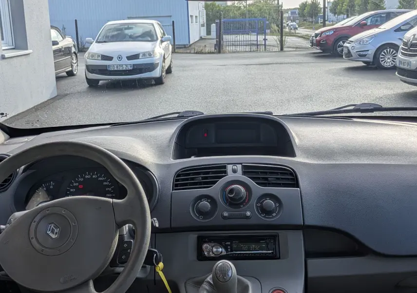 Vue intérieure avant du Renault Kangoo II 1.5 DCi 85 avec tableau de bord gris et volant à commandes audio intégrées.
