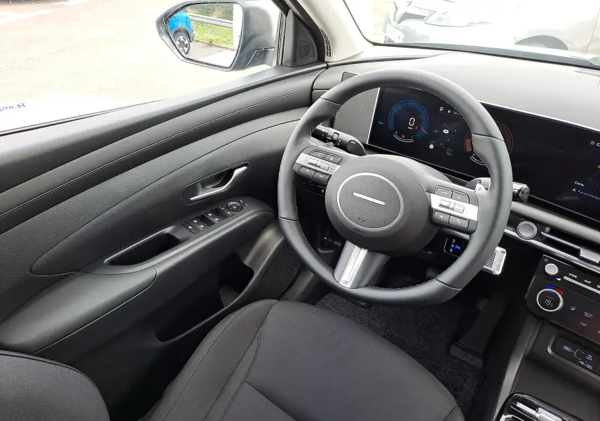 Intérieur côté conducteur du Hyundai Tucson 2025 gris, volant multifonction et tableau de bord numérique moderne.