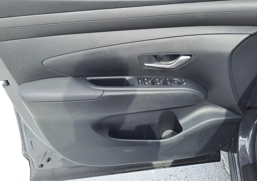 Vue rapprochée de la porte avant gauche grise du Hyundai Tucson 2025 avec commandes de vitres et poignée argentée.