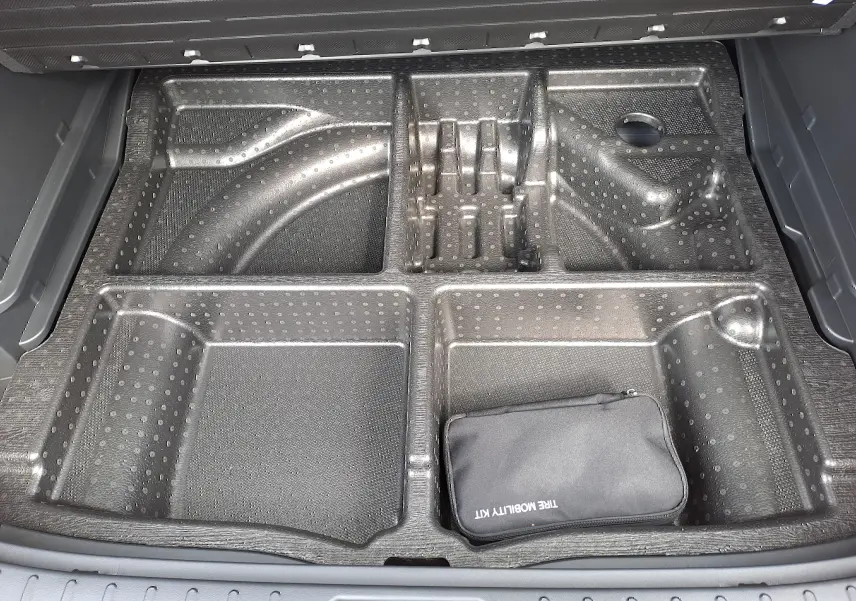 Compartiment de rangement sous le coffre du Hyundai Tucson 2025 gris Ecotronic, avec trousse de mobilité noire visible.