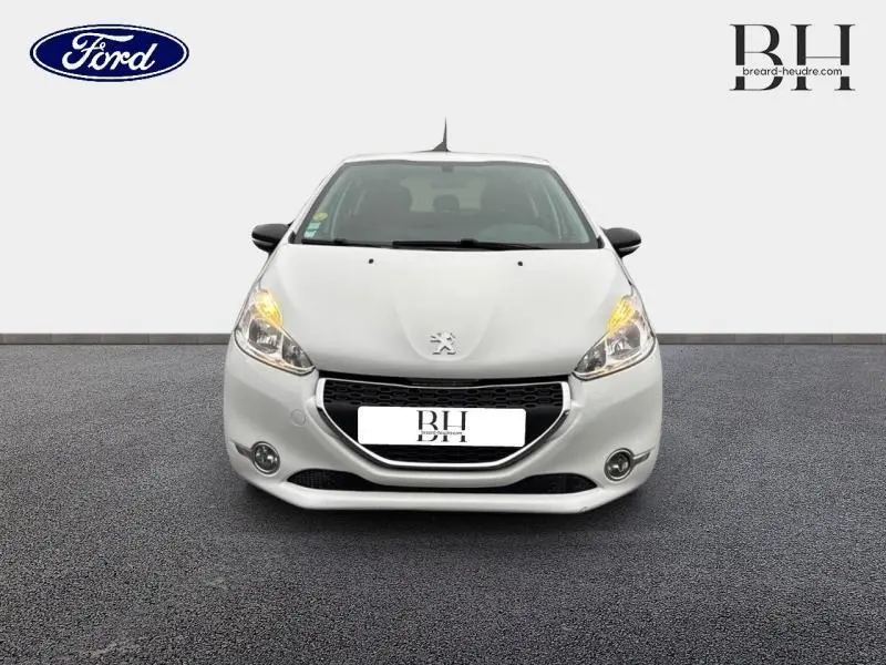 Vue frontale d'une Peugeot 208 blanche Banquise avec phares allumés sur fond neutre.