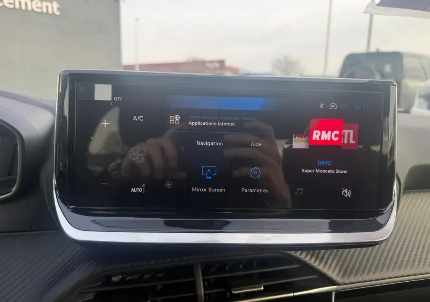 Écran tactile du tableau de bord de la Peugeot 208 Hybrid gris, affichant les options de navigation et radio RMC.