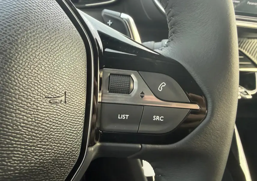 Gros plan sur les commandes gauche du volant noir du Peugeot 208 Hybrid 110 e-DCS6 Allure gris, avec boutons multifonctions.