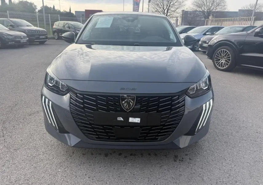 Vue frontale d'une Peugeot 208 Hybrid 110 gris métallisé, avec calandre noire et feux diurnes LED en forme de griffes.
