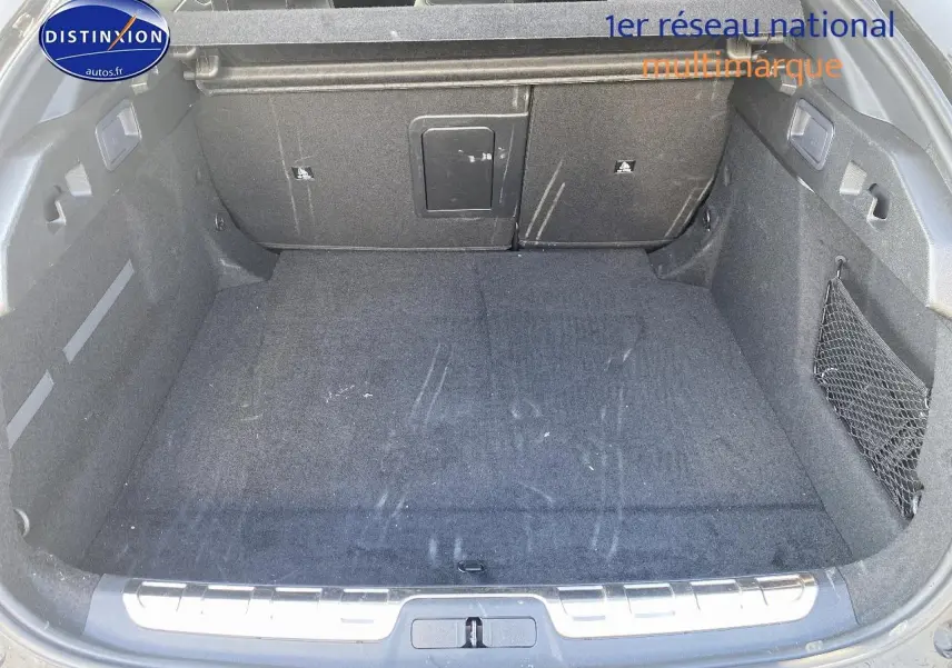 Vue plongeante sur le coffre spacieux et noir du Peugeot 408 Hybrid 145 GT e-dcs6, avec filet de rangement latéral.