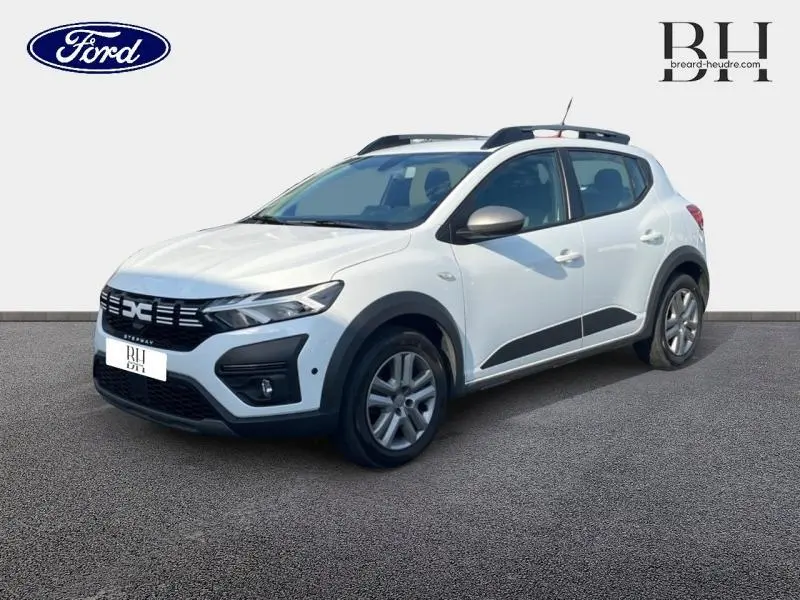 Vue 3/4 avant droite d'une Dacia Sandero Stepway blanche avec barres de toit et protections noires sur les bas de caisse.