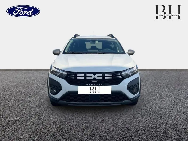Vue frontale d'une Dacia Sandero Stepway blanche 2023 avec calandre noire et barres de toit visibles.