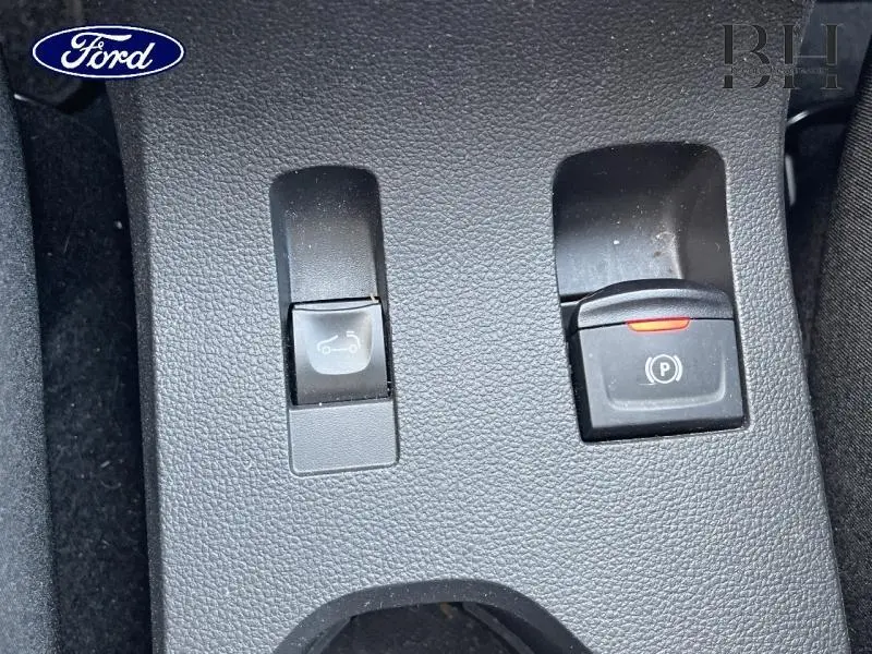 Gros plan sur les commandes de frein à main électrique et ouverture de coffre d'une Dacia Sandero blanche.