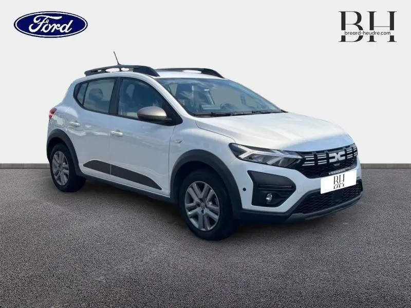 Vue 3/4 avant droit d'une Dacia Sandero blanche avec barres de toit et détails noirs contrastants sur les bas de caisse.