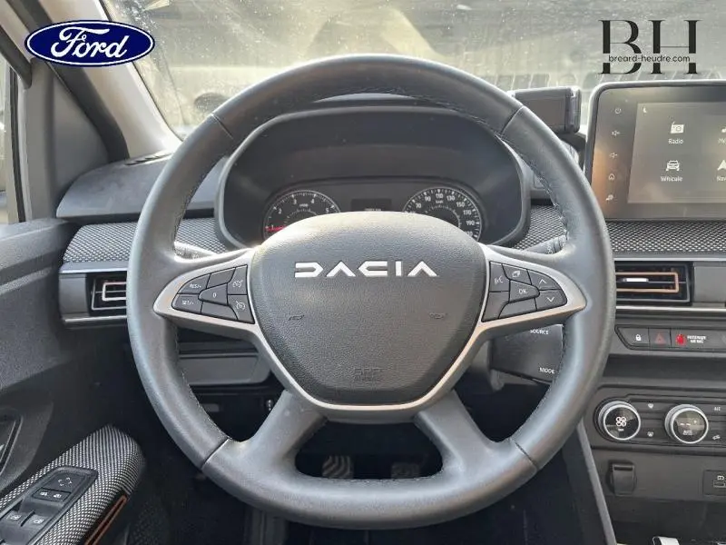 Vue intérieure centrée sur le volant noir de la Dacia Sandero 2023 avec tableau de bord et écran tactile visibles.