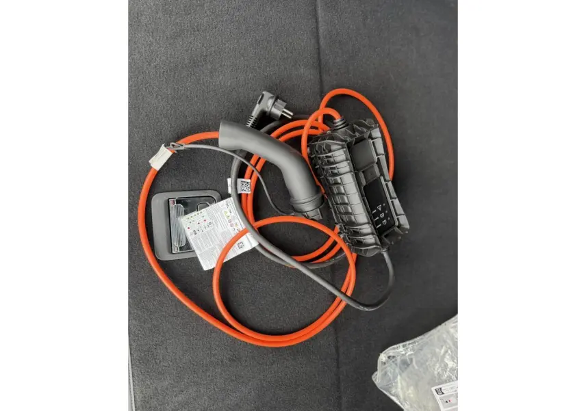 Câble de recharge orange et noir posé dans le coffre d’un Peugeot 3008 Plug-in Hybrid 2024 noir Perla.