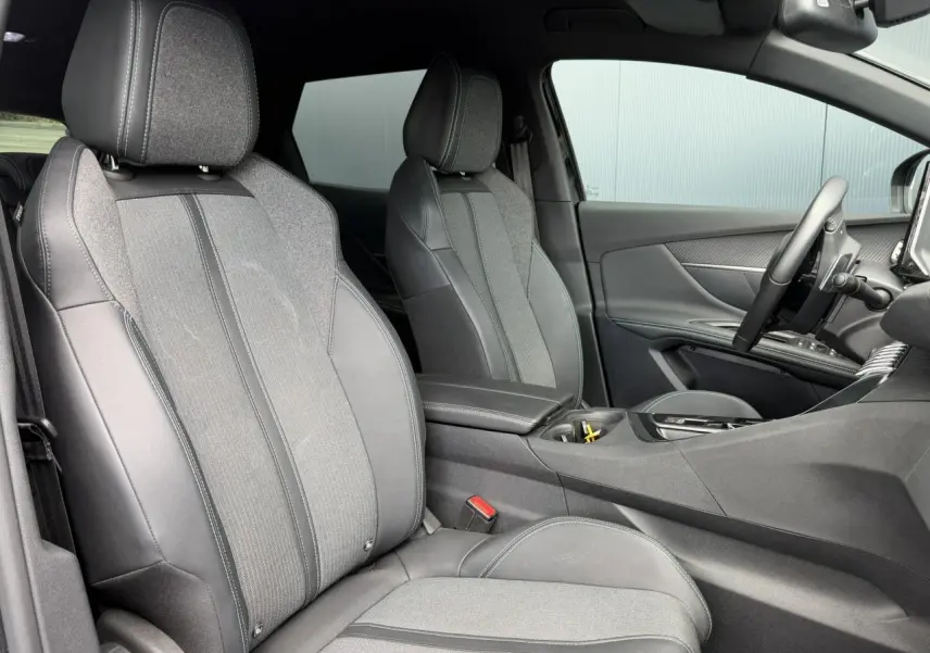 Vue intérieure côté conducteur du Peugeot 3008 2024 noir Perla, sièges bi-matière cuir et tissu gris, accoudoir central ouvert.