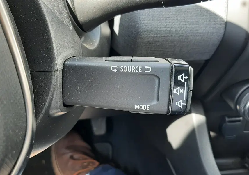 Gros plan sur la commande au volant gauche de la Renault Clio V, avec boutons source et mode visibles, intérieur gris.