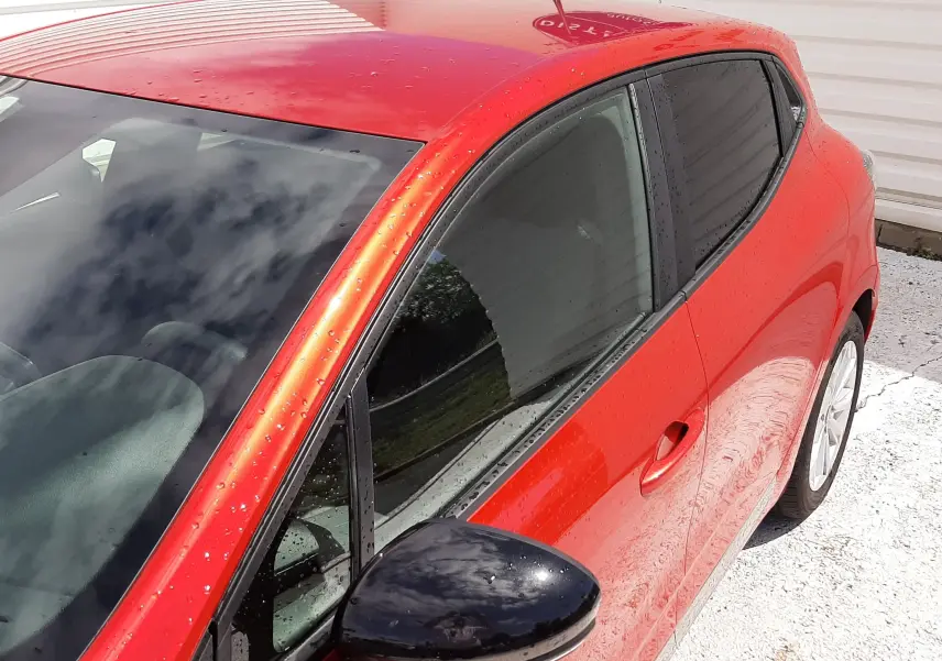 Vue 3/4 avant droit de la Renault Clio V rouge flamme avec rétroviseur noir et vitres teintées.