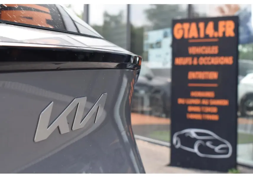 Gros plan sur l'arrière gauche gris loup du Kia Sportage 2026 avec logo Kia en relief, devant une vitrine de concession.