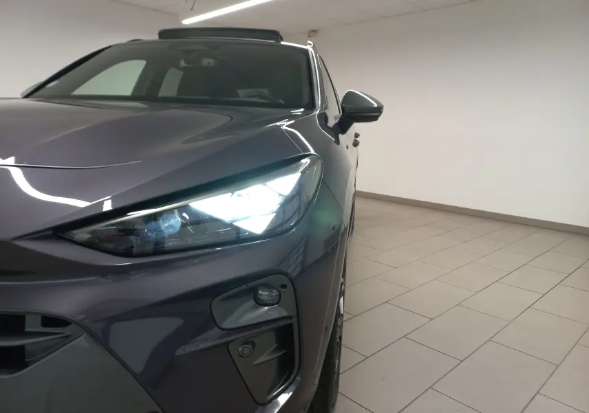 Gros plan sur l'avant droit violet intersidéral du CUPRA TERRAMAR 2025 avec phare allumé dans un intérieur neutre.