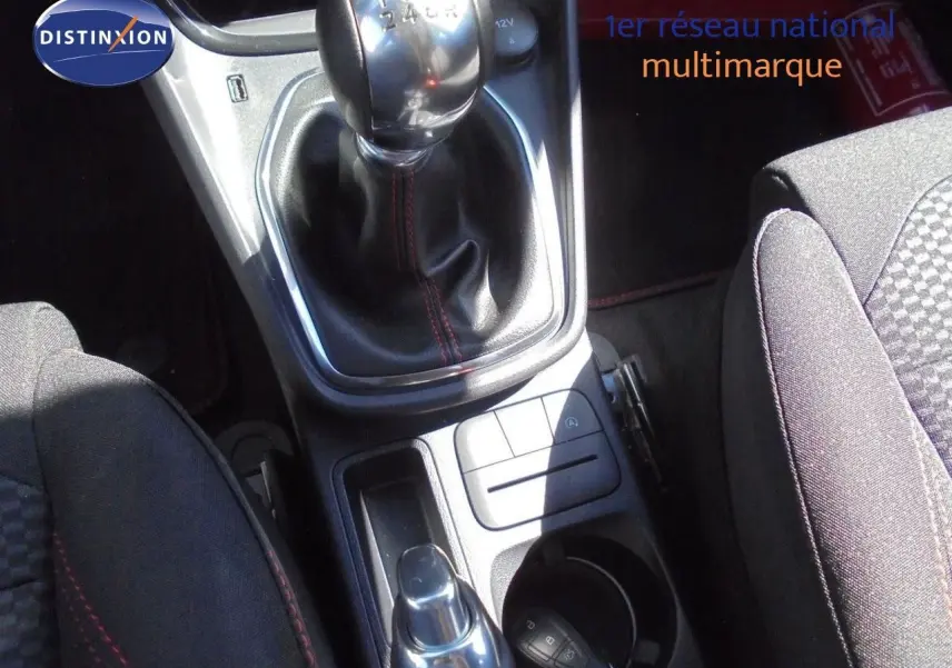 Gros plan sur la console centrale du Ford Puma 2022, montrant levier de vitesse manuel et sièges tissu noir avec surpiqûres rouges.