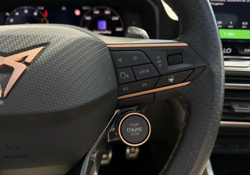 Gros plan sur le volant perforé noir avec logo CUPRA cuivre et bouton Start Engine Stop dans un intérieur moderne.