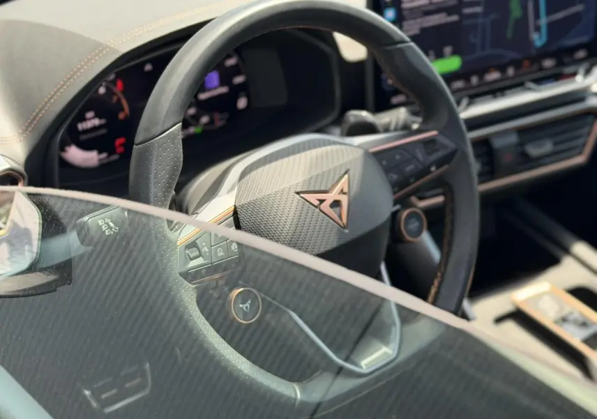 Gros plan sur le volant noir perforé avec logo CUPRA cuivré et tableau de bord numérique partiellement visible.