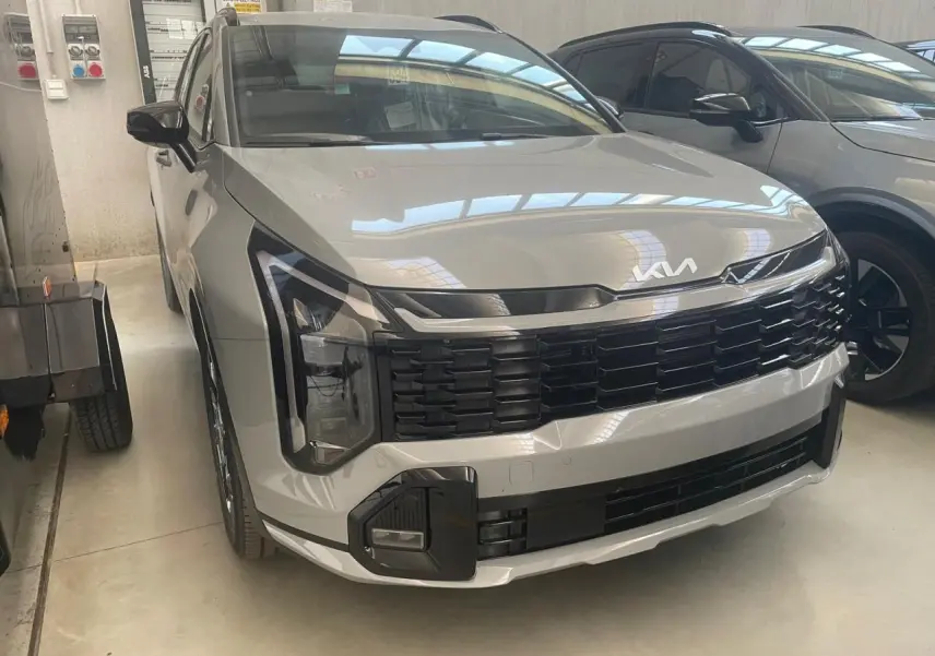 KIA Sportage Hybride gris lunaire vu de face 3/4 gauche, avec calandre noire et signature lumineuse verticale distinctive.