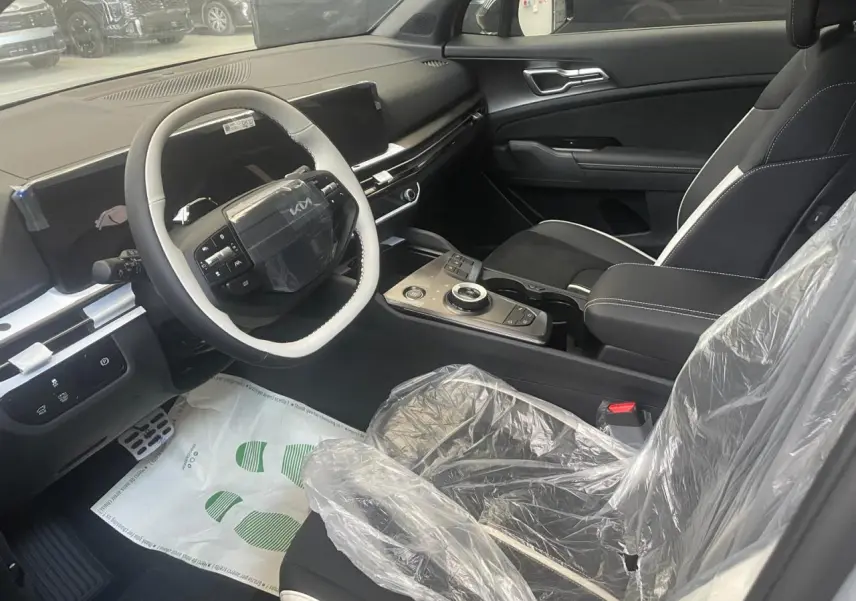 Intérieur avant droit du KIA Sportage 2026 gris lunaire, volant multifonction, écran tactile et siège protégé par housse plastique.