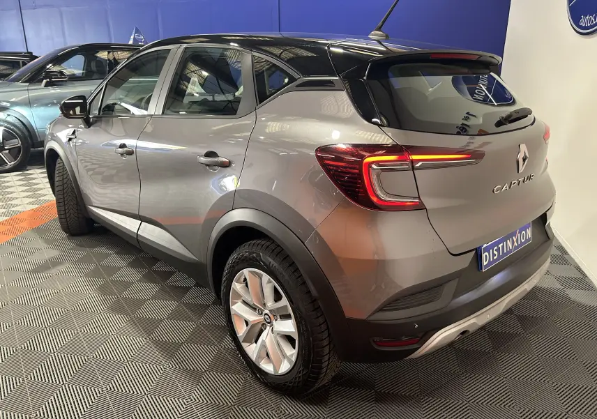 Vue 3/4 arrière droite d'un Renault Captur gris 2022 avec toit noir et feux LED allumés en intérieur showroom.