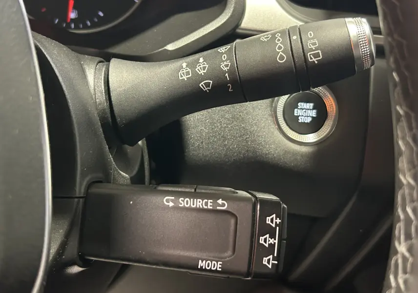 Gros plan intérieur sur les commandes au volant et bouton start/stop du Renault Captur gris 2022, version essence manuelle.