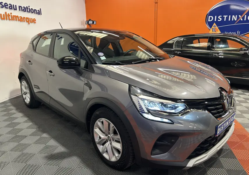 Renault Captur II TCE 90 gris vue 3/4 avant droit, phares allumés, calandre noire et jantes argentées.