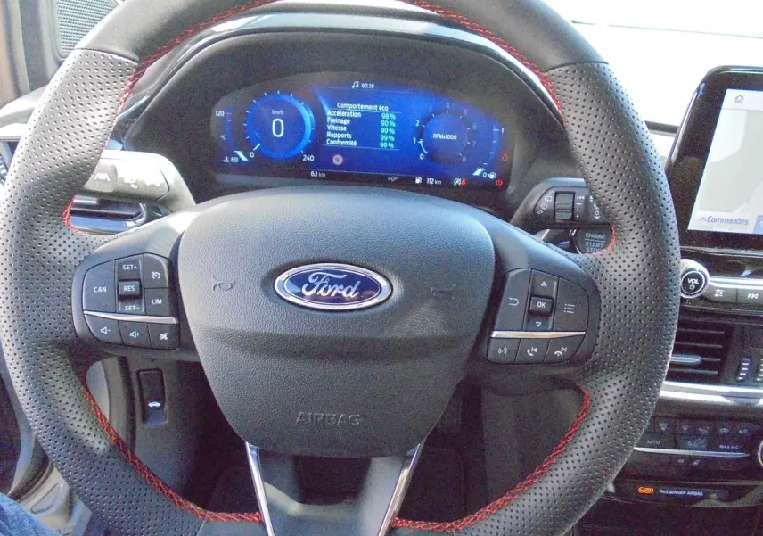 Vue rapprochée du volant perforé avec surpiqûres rouges et tableau de bord digital bleu d'une Ford Puma gris Solar Metal 2022.