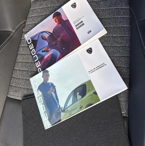 Image montrant deux brochures Peugeot posées sur un siège de voiture gris, avec détails de textures et coutures visibles.