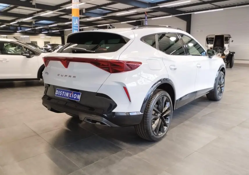 Vue 3/4 arrière droite du CUPRA Formentor blanc Nevada avec jantes noires et éléments noirs contrastants en intérieur showroom.