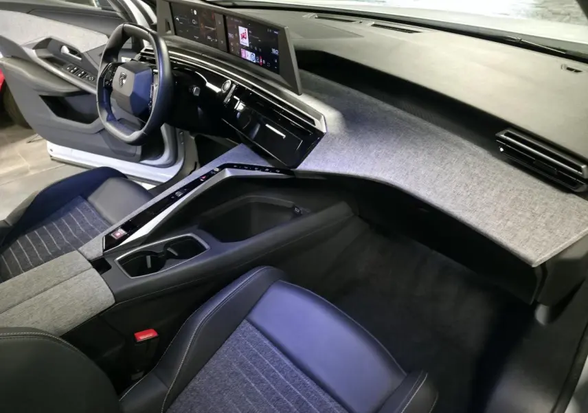Intérieur avant droit du Peugeot 3008 2025 avec tableau de bord gris chiné et sièges tissu bleu et cuir noir.