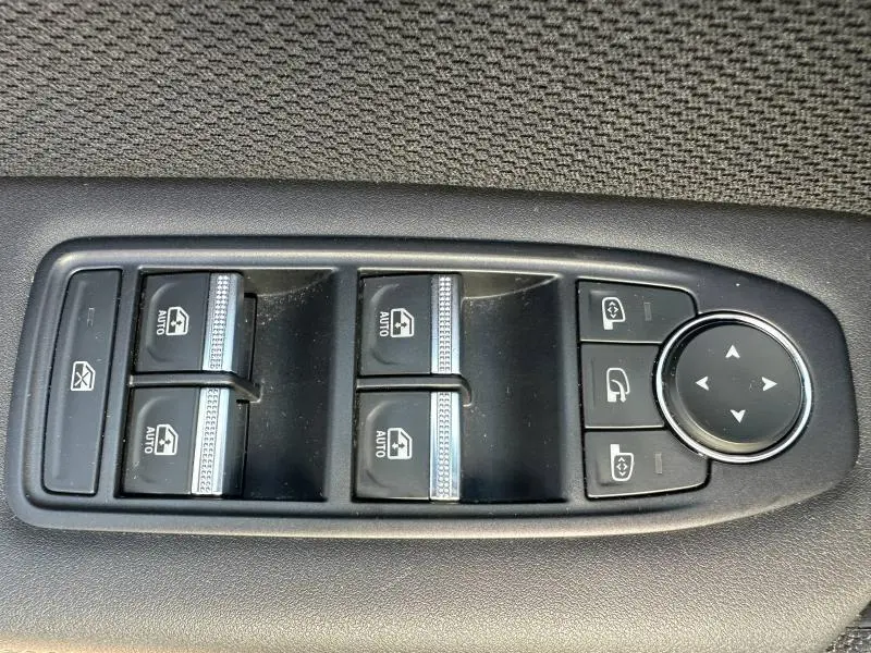 Gros plan sur les commandes de lève-vitres et rétroviseurs sur la porte intérieure d'une Renault Symbioz rouge.