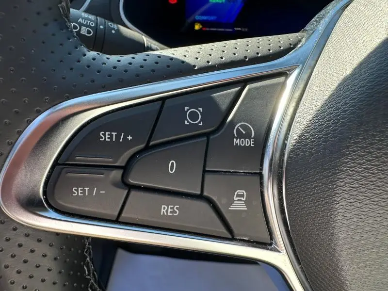 Gros plan sur les commandes multifonctions noires du volant perforé de la Renault Symbioz rouge, avec boutons de régulateur et mode.
