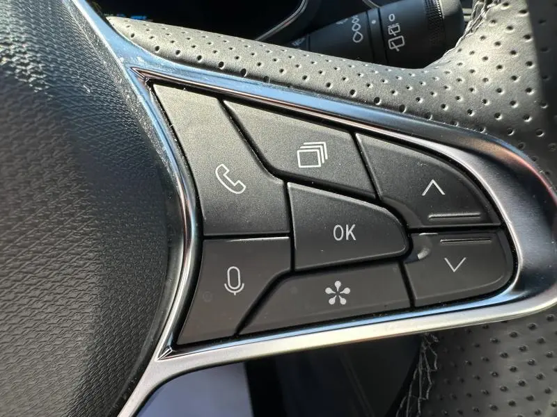 Gros plan sur les commandes multifonctions noires du volant perforé de la Renault Symbioz rouge 2025.