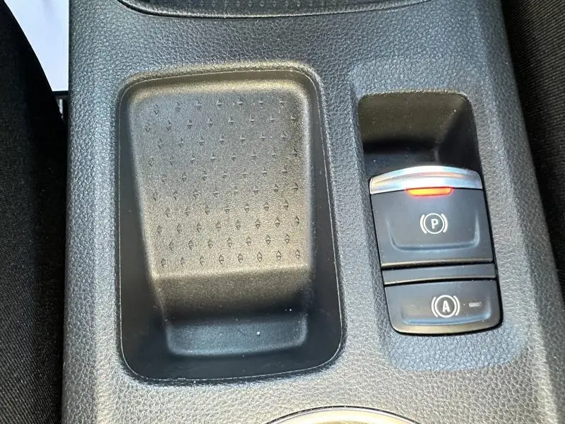 Gros plan sur la console centrale noire du Renault Symbioz rouge, avec bouton de frein à main électronique et espace de rangement.