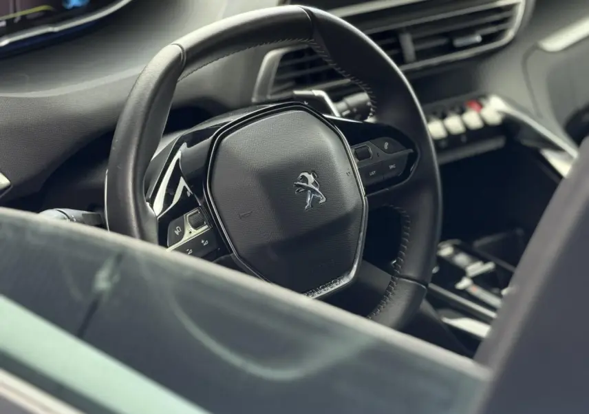Vue rapprochée du volant noir cuir Mistral du Peugeot 3008 Plug-in Hybrid avec commandes intégrées et tableau de bord partiel.