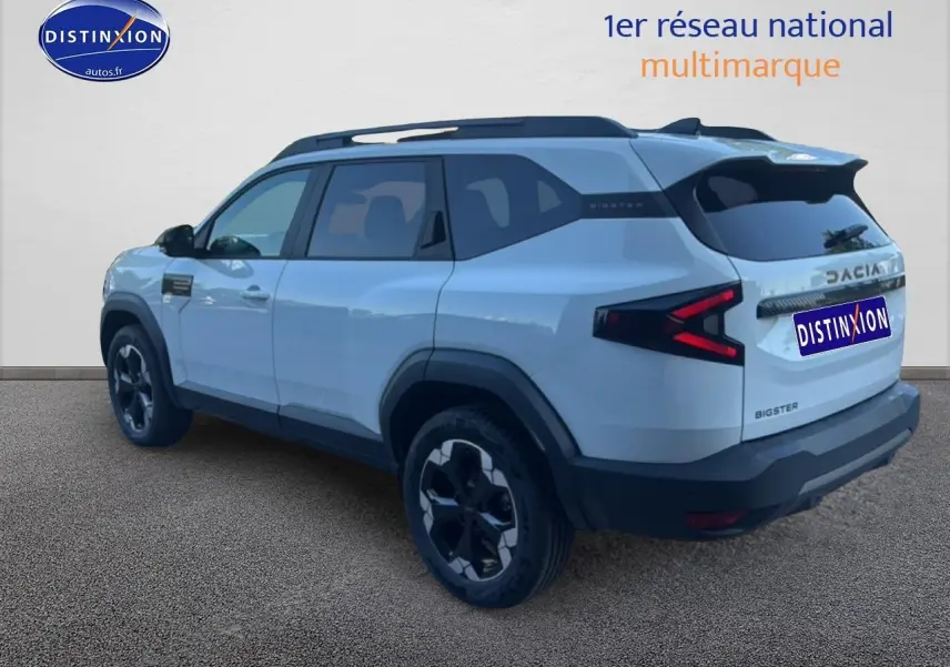 Vue 3/4 arrière droite d'un Dacia Bigster blanc avec barres de toit et jantes alu noires.