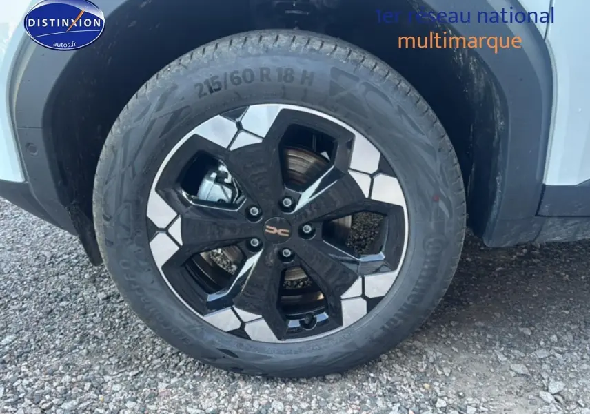 Gros plan sur la roue avant droite du Dacia Bigster blanc avec jante alu noire et argentée au design hexagonal.
