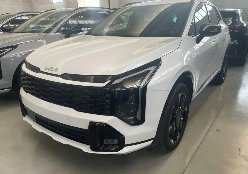 Vue 3/4 avant d'un KIA SPORTAGE hybride blanc 2026 avec calandre noire et jantes noires distinctives.