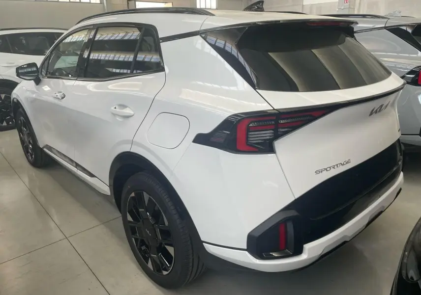 Vue 3/4 arrière droite du KIA Sportage blanc hybride 2026 avec jantes noires et feux arrière LED distinctifs.