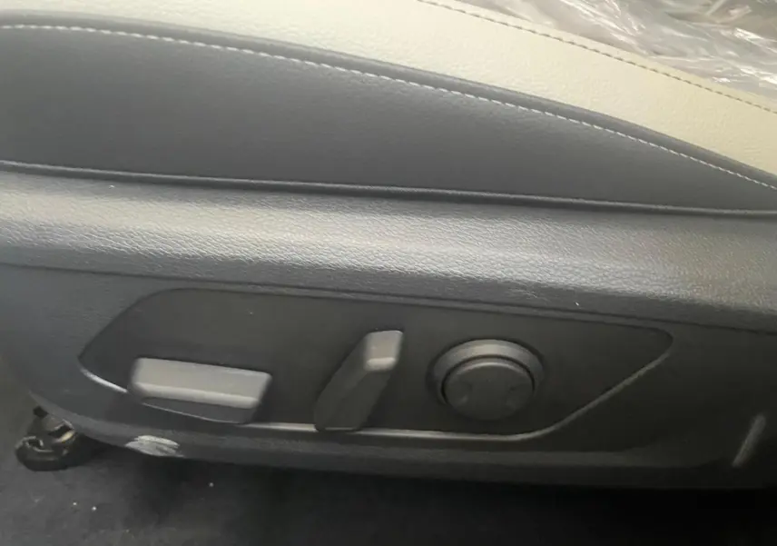 Détail des commandes de réglage électrique du siège avant en cuir noir du Kia Sportage Hybride blanc 2026.