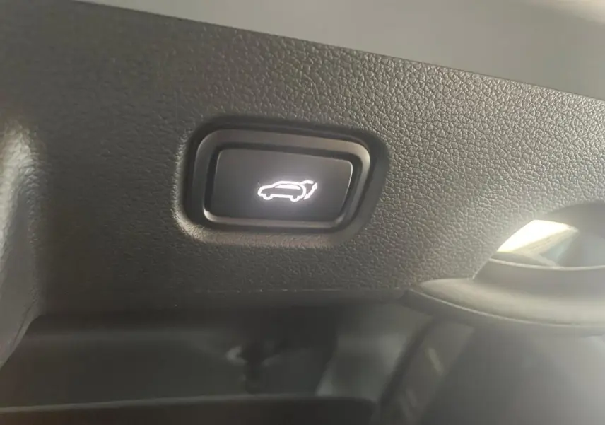 Bouton intérieur noir avec symbole blanc d'ouverture du coffre sur KIA SPORTAGE Hybride 2026, vue rapprochée du tableau de bord.