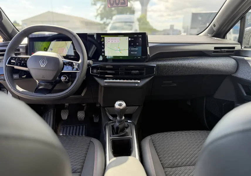 Vue intérieure frontale de la Renault Clio VI TCe 115 Techno avec tableau de bord moderne et levier de vitesse manuel.