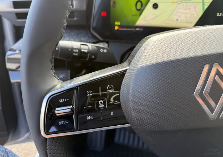 Gros plan sur la partie gauche du volant gris d’une Renault Clio VI TCe 115 Techno avec commandes de régulateur et tableau de bord numérique.
